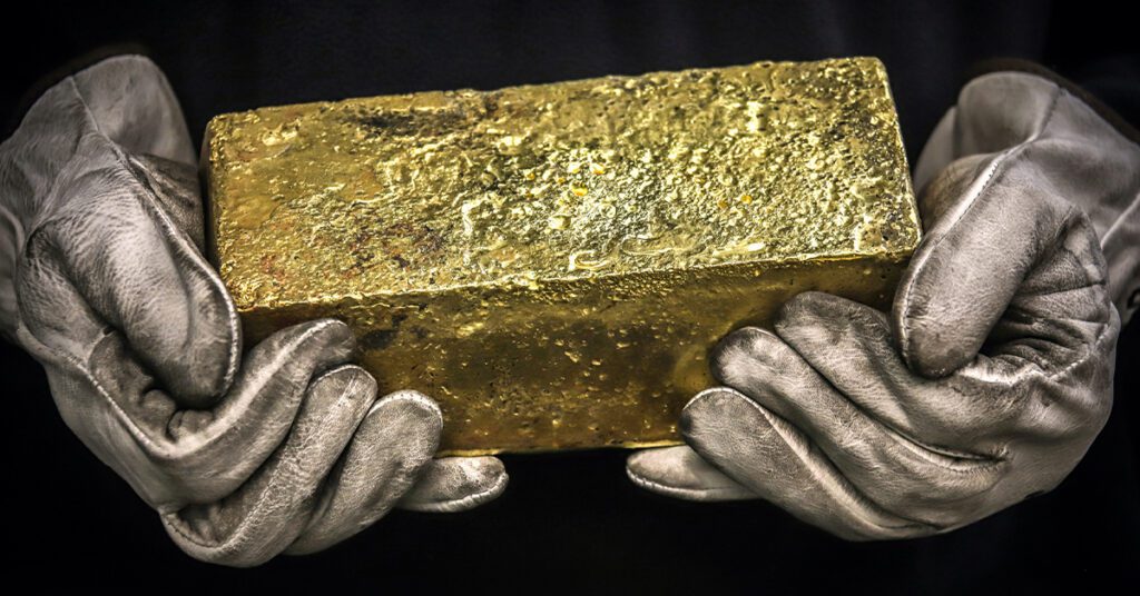 man holding shiny gold bar with gloves on