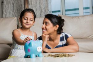 child putting coins into piggy bank with mum watching