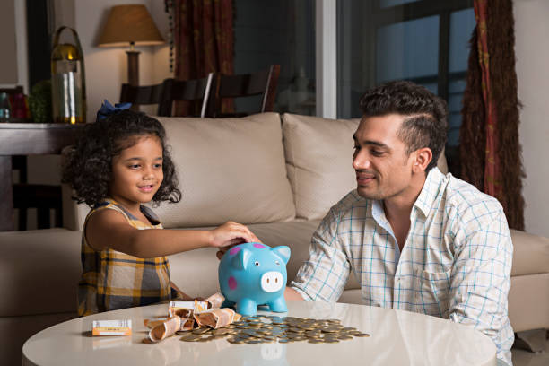 portrait of dad helping young daughter put savings into a piggy bank